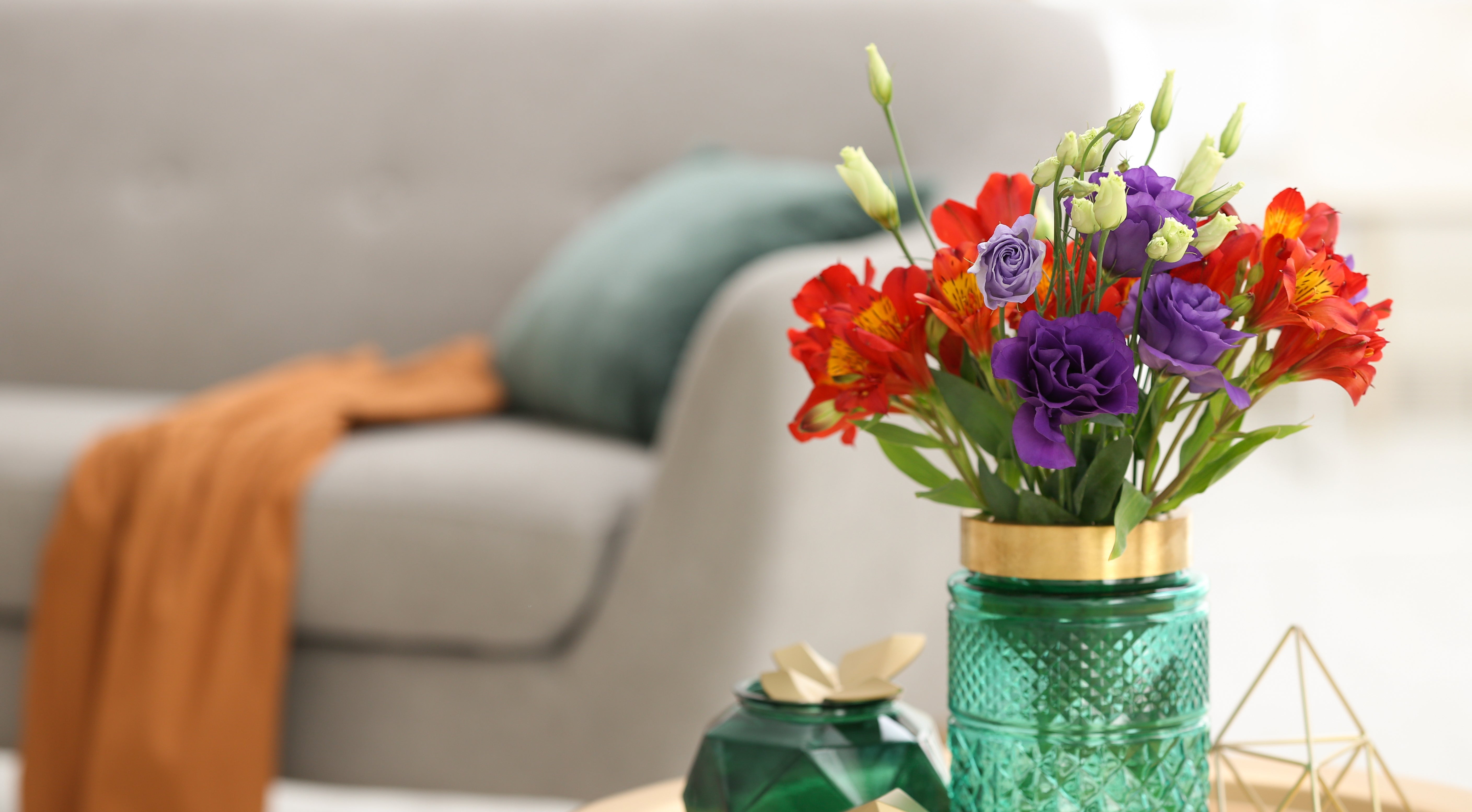 Colorful flowers in a green vase on a coffee table with a couch in the background